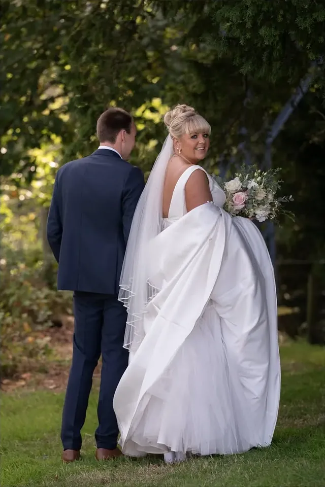 Couple walking into woodland, the bride holding her dress