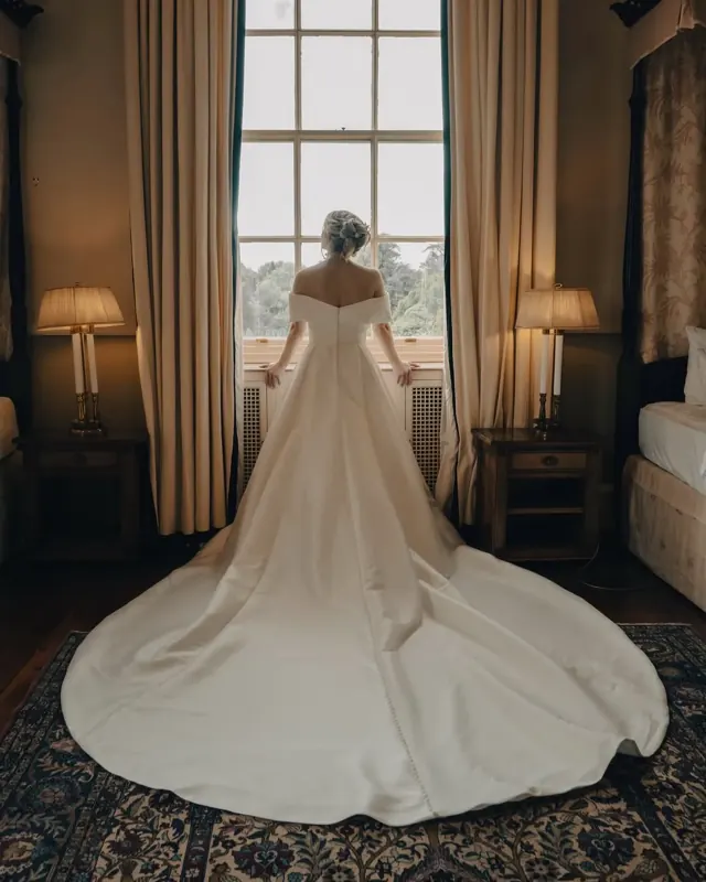 Bride from behind in a long-trained gown at a tall window