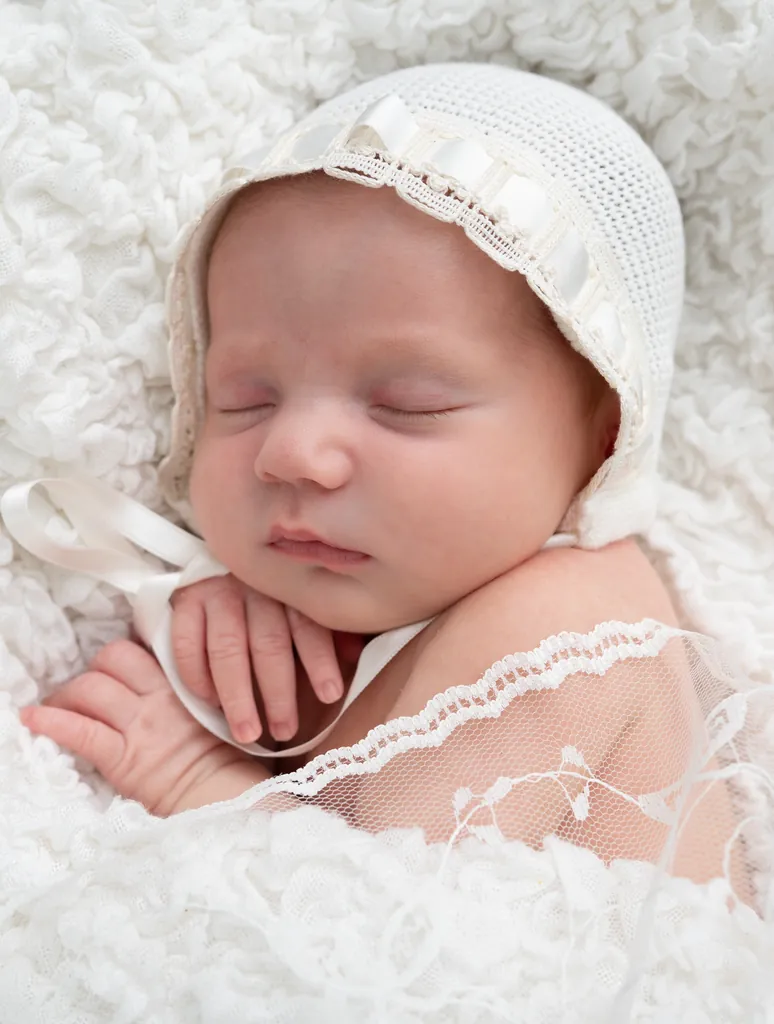 Sleeping newborn in a lace bonnet on soft white fur