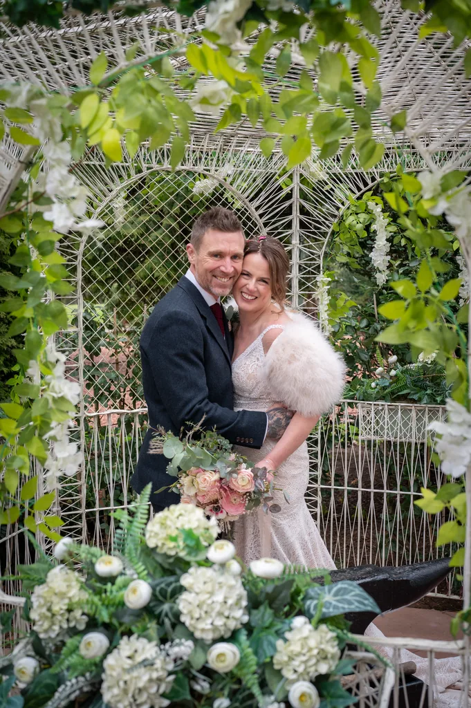 Bride and groom standing together beside a flower-trimmed white gate