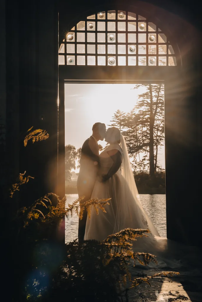 Bride and groom silhouetted in a grand doorway framed by dark foliage