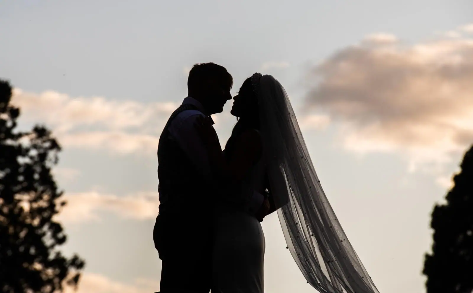 Silhouette of a couple about to kiss against a soft evening sky