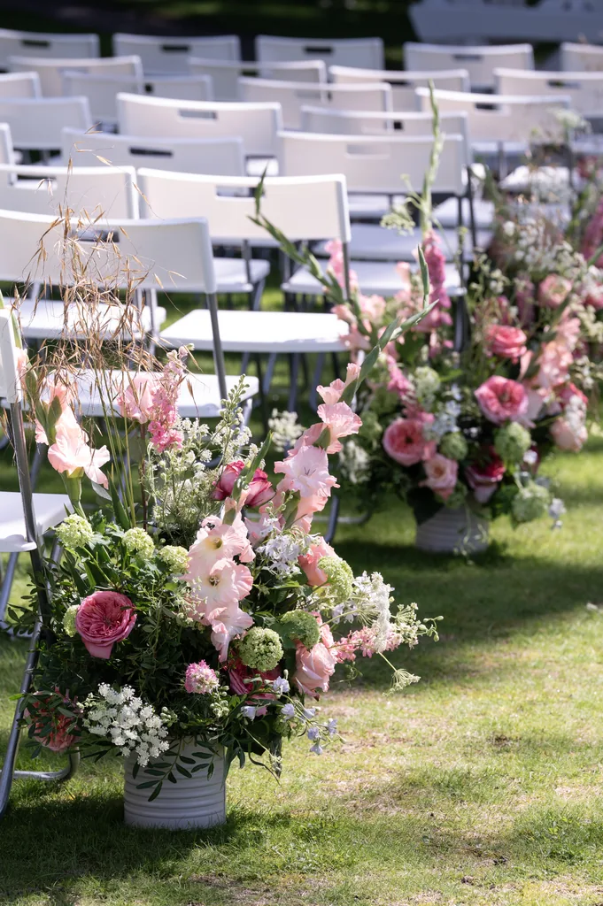 White ceremony chairs lined up outdoors with floral aisle arrangements