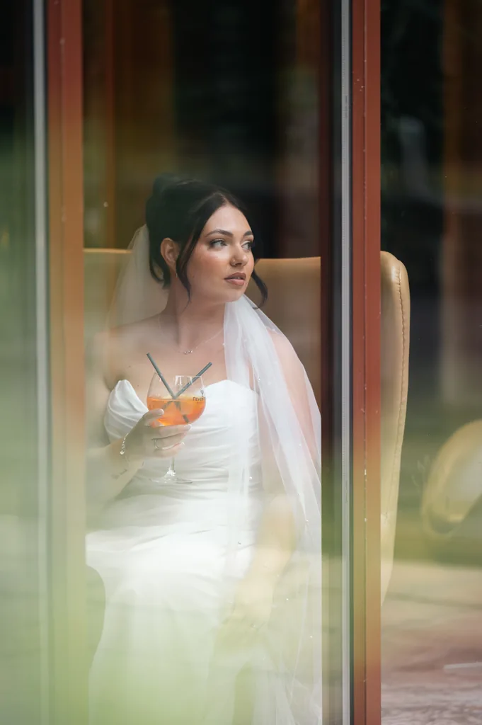 Bride holding a glass of champagne seen through a paned glass door