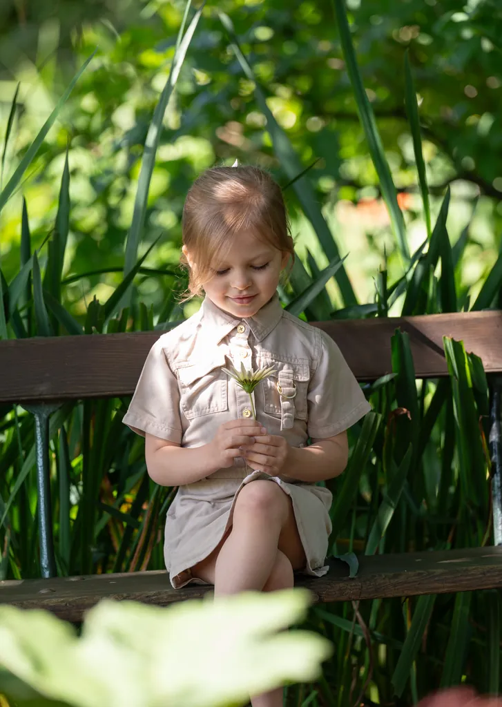 Little girl holding flowers on a garden bench among tall leaves