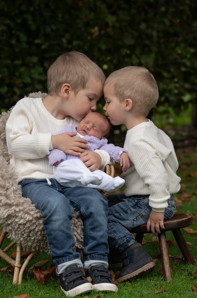Two young brothers cuddling a baby on a seat in the garden