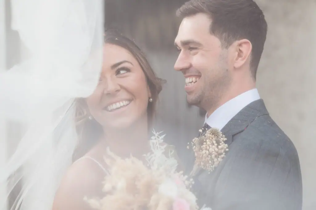 Bride and groom smiling at each other through her veil