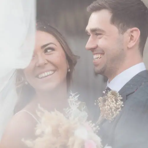 Bride and groom smiling at each other through her veil