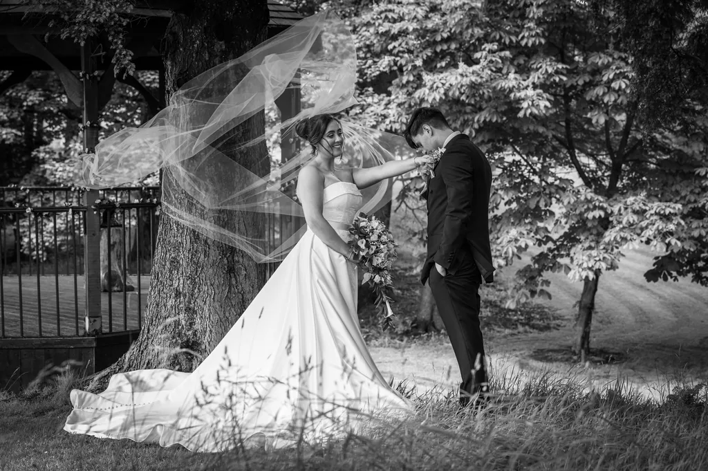 Black-and-white portrait of newlyweds in woodland with the bride’s long veil blowing in the wind
