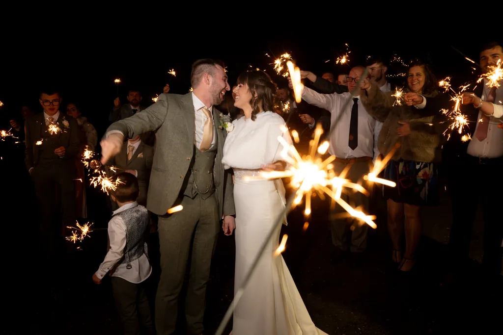 Newlyweds walking through a nighttime tunnel of guests holding lit sparklers