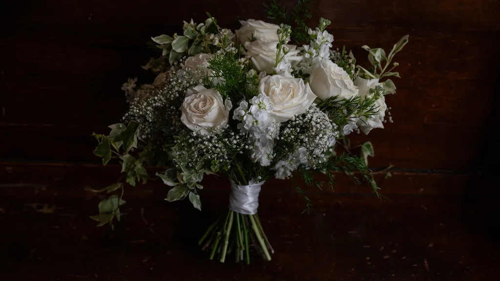 Wedding bouquet of white roses and greenery resting on dark wood