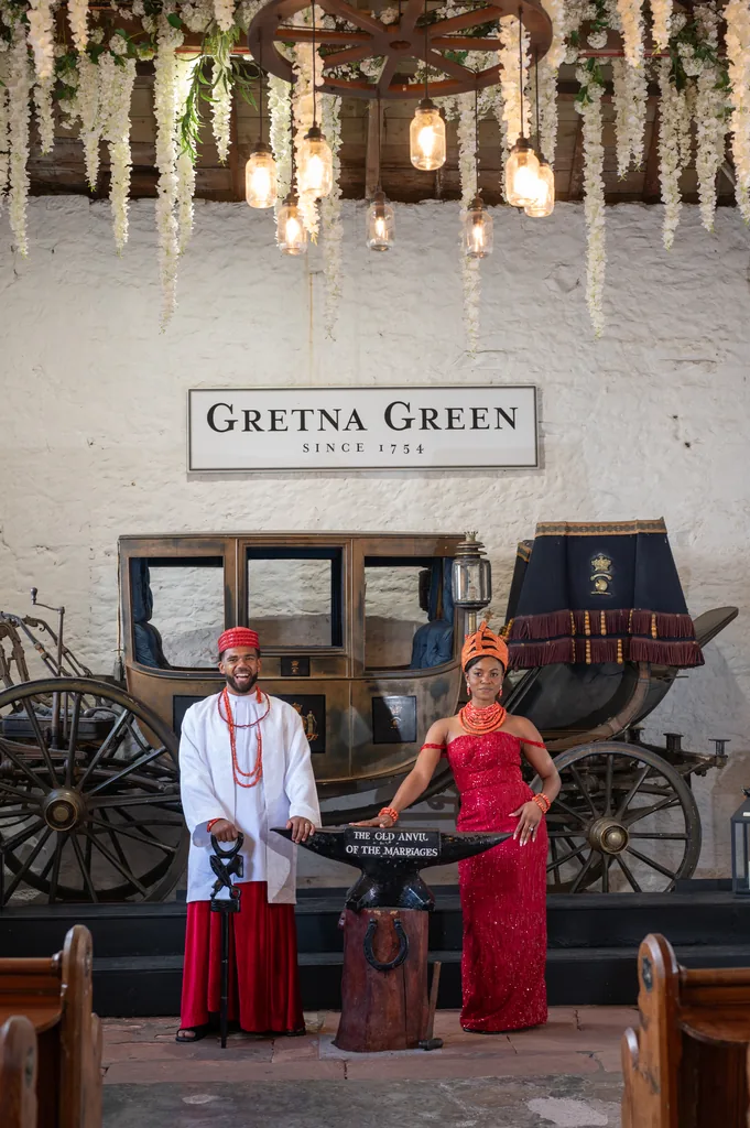 Bride and groom posing beside a vintage carriage and anvil at Gretna Green
