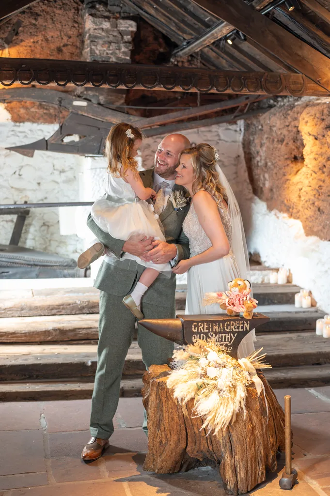 Bride, groom and young child sitting together on rustic wooden steps