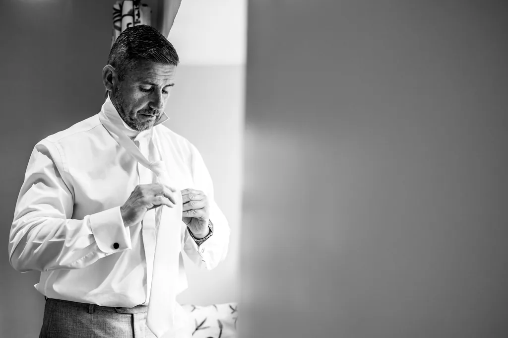 Black-and-white portrait of a groom adjusting his cufflinks