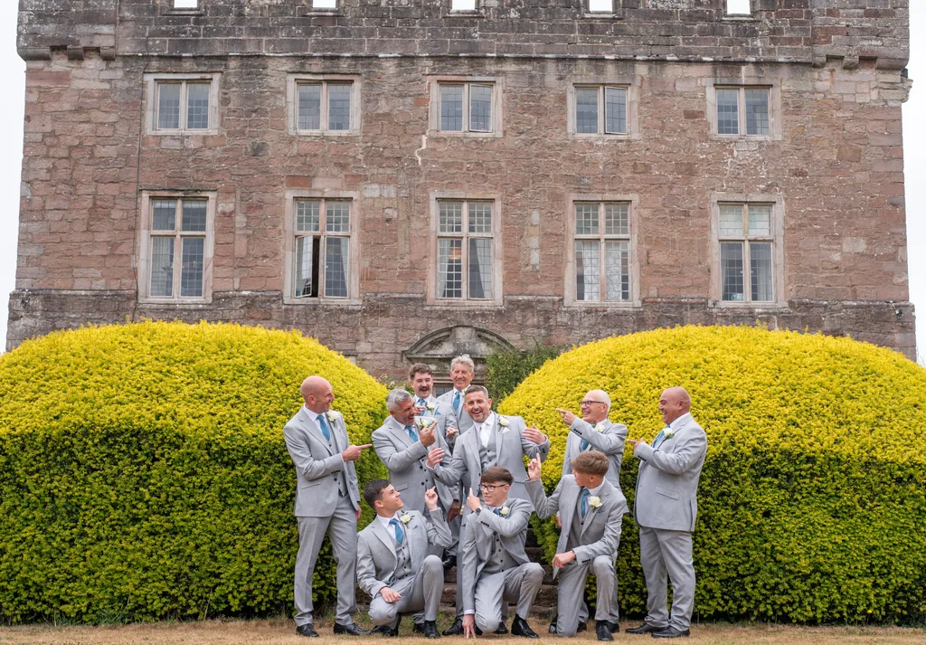 Groomsmen in grey suits posing in front of a red-sandstone manor house