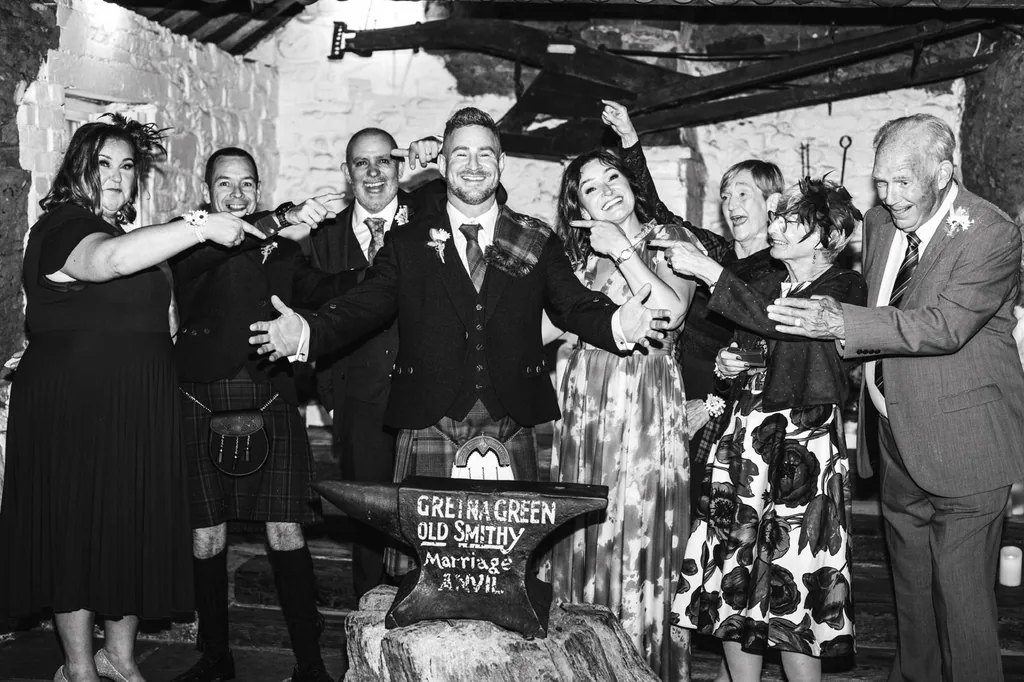 Black-and-white photo of the wedding party gathered round the anvil at the Old Smithy, Gretna Green