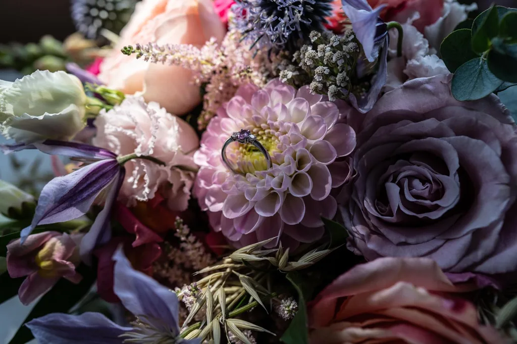 Close-up of a purple and pink bridal bouquet with a wedding ring resting on it