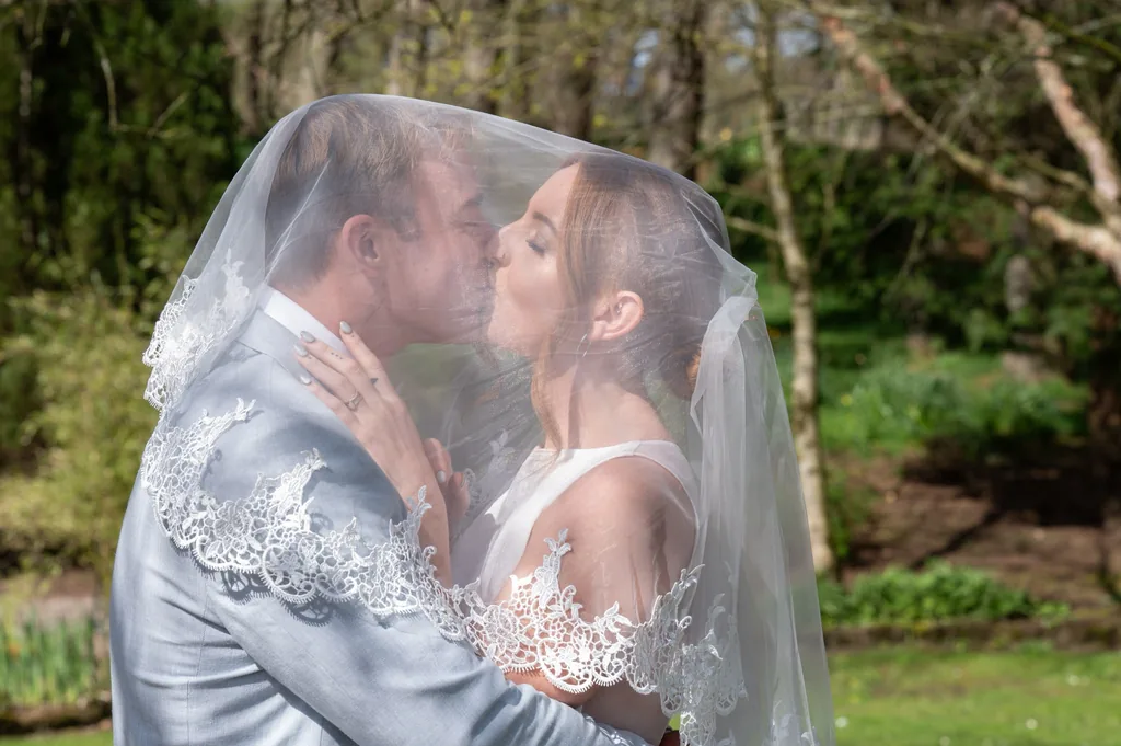 Bride and groom kissing under her veil in the woods