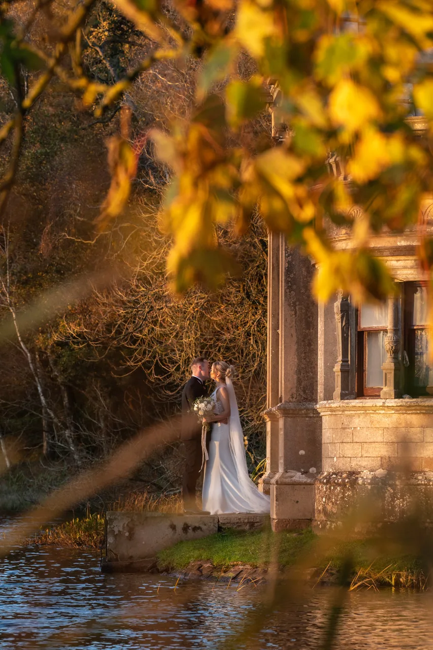 Rachel and Scott kissing in the gardens at Kinmount House framed by autumn leaves